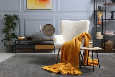 Photo of Living room interior with comfortable armchair, blanket and side table