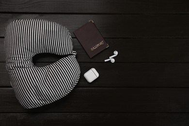 Photo of Striped travel pillow, passport and earphones on dark wooden background, flat lay. Space for text