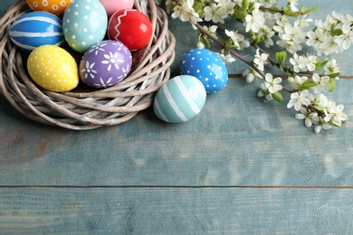 Photo of Painted Easter eggs in nest and blossoming branches on table, view from above. Space for text