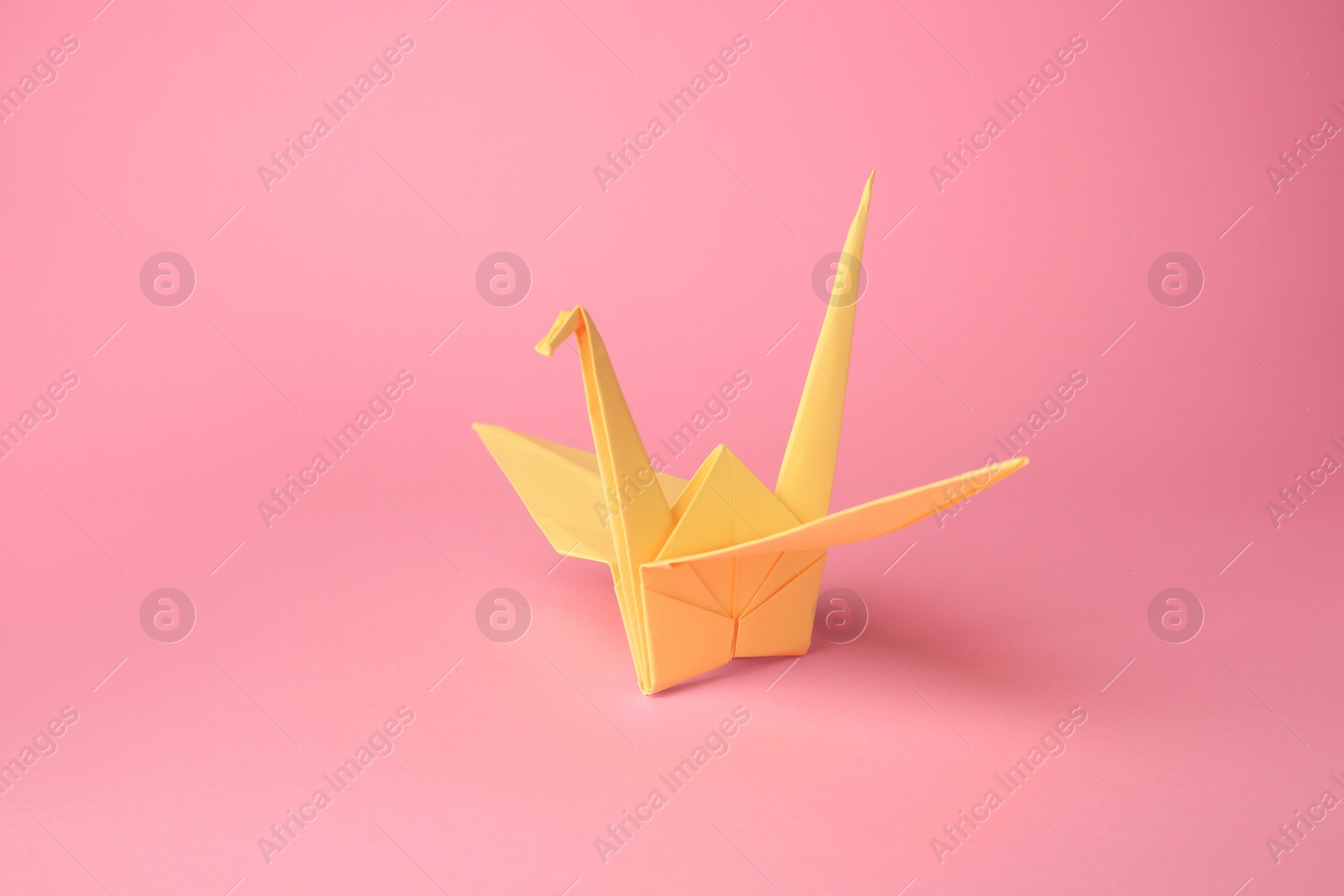 Photo of Origami art. Handmade paper crane on pink background