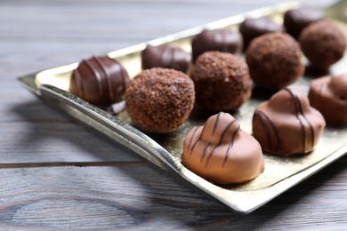 Photo of Metal tray with tasty chocolate candies on wooden table, closeup
