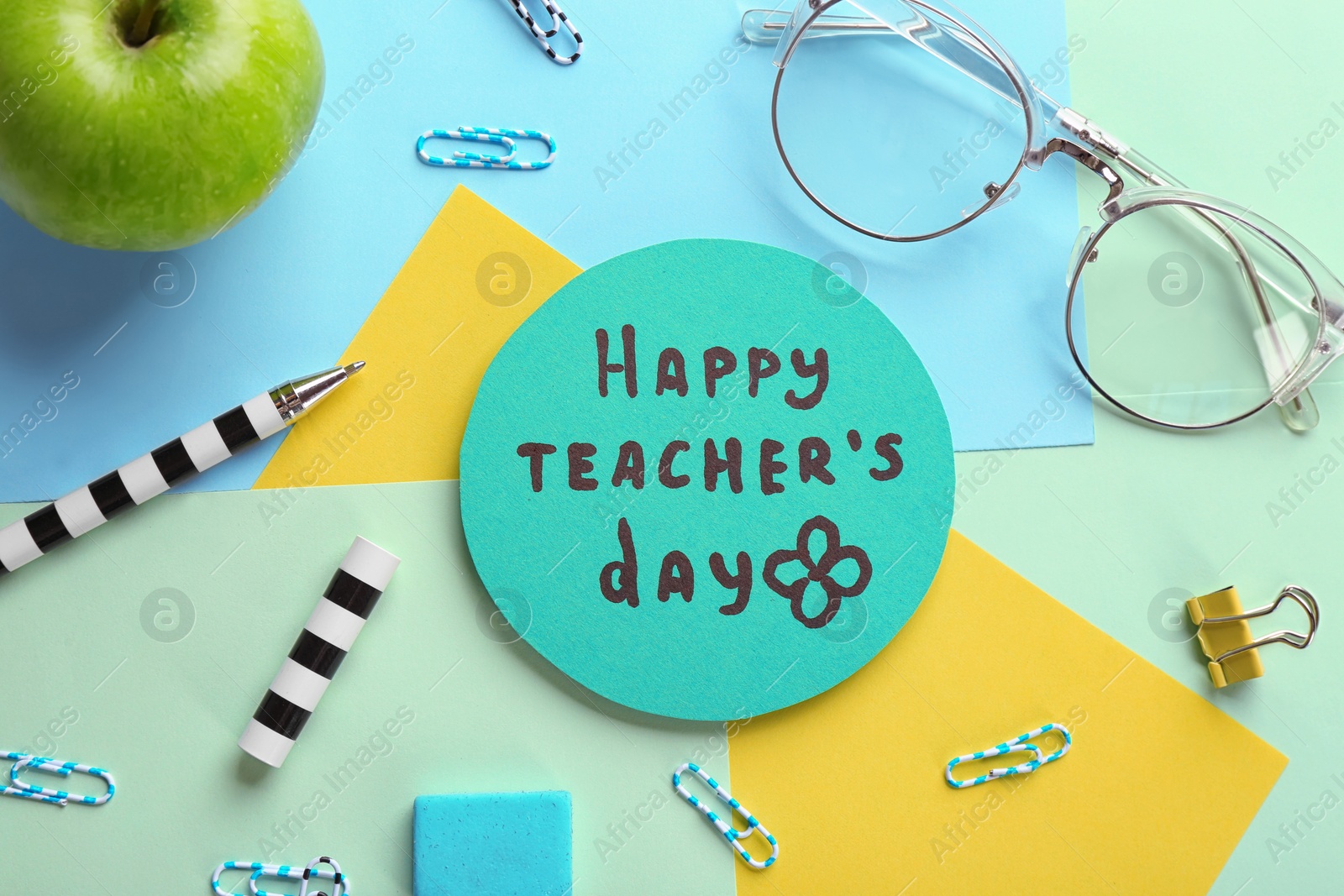 Photo of Paper with inscription HAPPY TEACHER'S DAY and stationery on color background