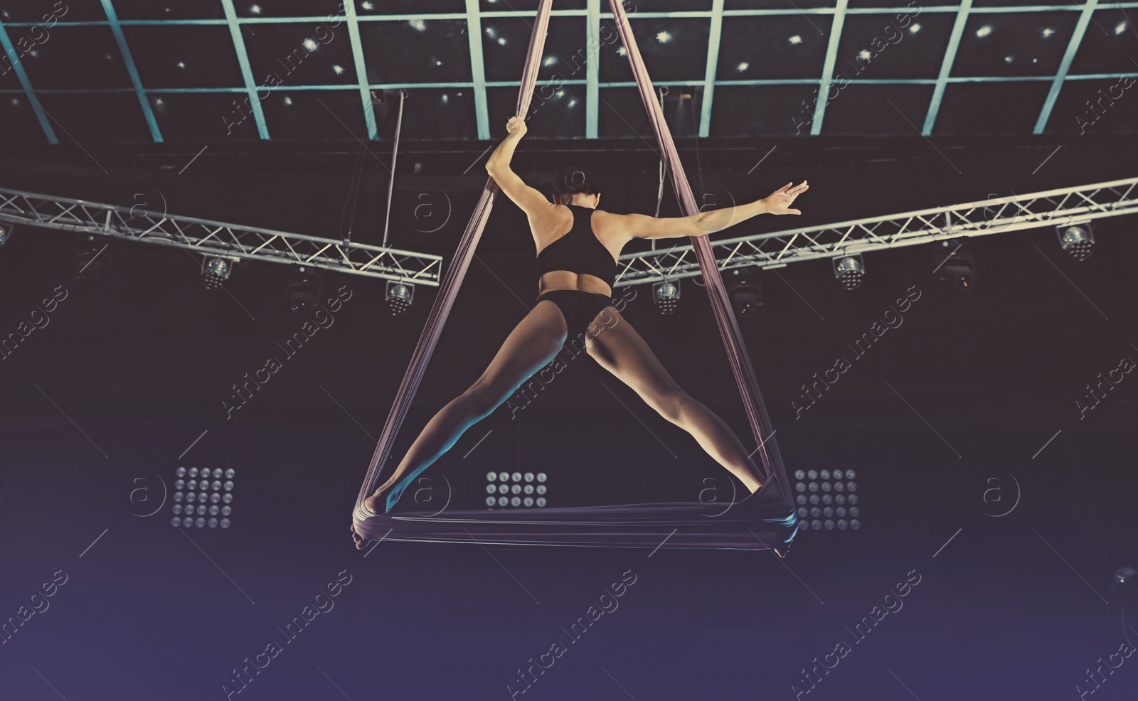 Photo of Young woman performing acrobatic element on aerial silk indoors