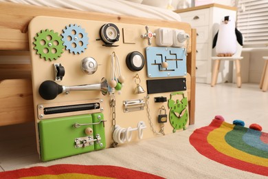 Photo of Busy board on floor near bed indoors. Baby sensory toy