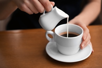 Photo of Woman pouring milk into cup of coffee on table