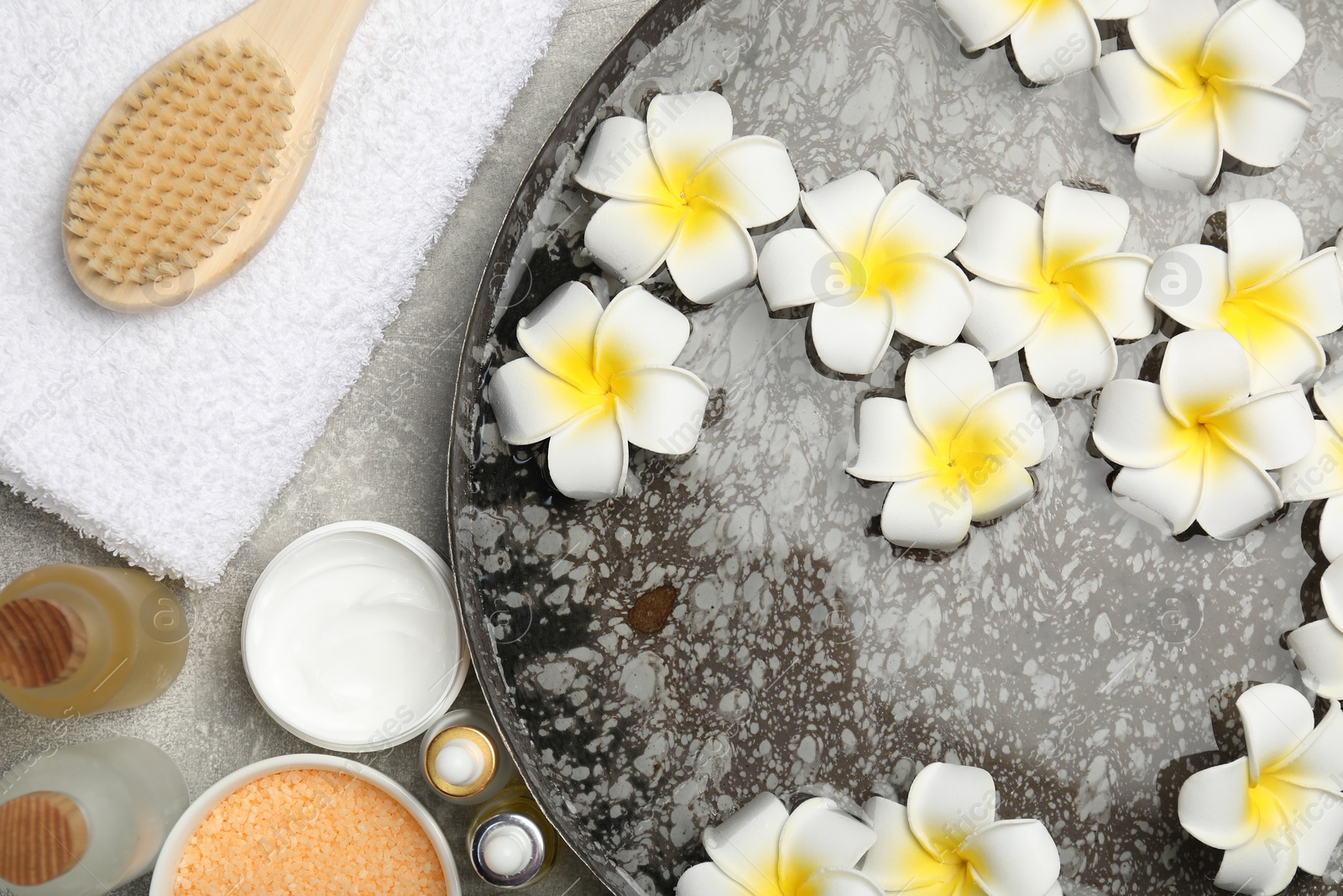 Photo of Bowl of water with flowers and different spa supplies on light grey table, flat lay