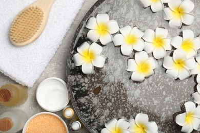 Photo of Bowl of water with flowers and different spa supplies on light grey table, flat lay