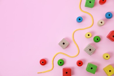 Wooden pieces and string for threading activity on pink background, flat lay and space for text. Educational toy for motor skills development