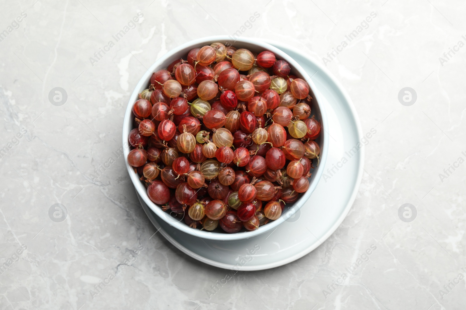 Photo of Bowl full of ripe gooseberries on light grey marble table, top view