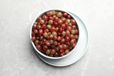 Bowl full of ripe gooseberries on light grey marble table, top view