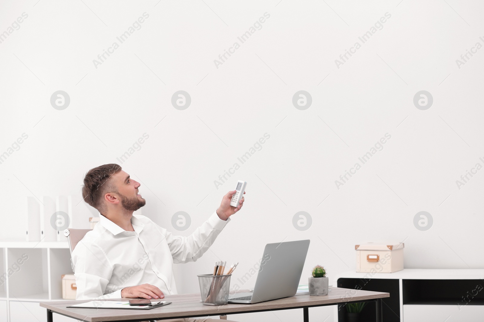 Photo of Young man with air conditioner remote in office