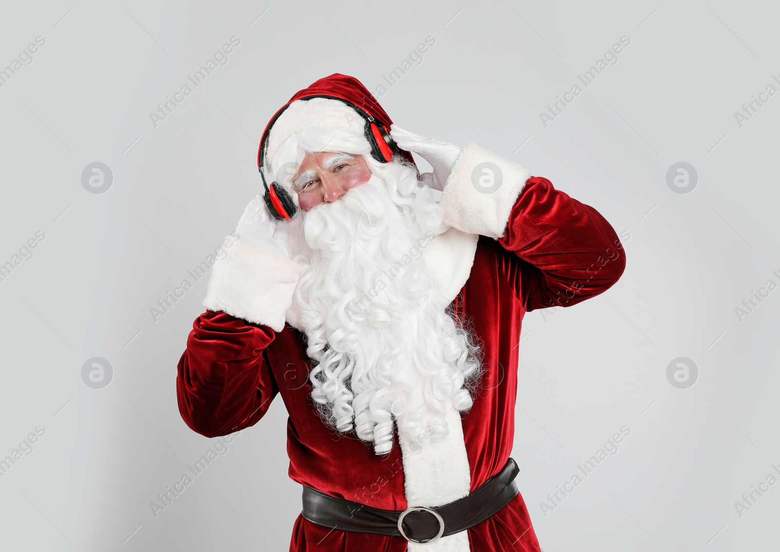 Photo of Santa Claus with headphones listening to Christmas music on light grey background