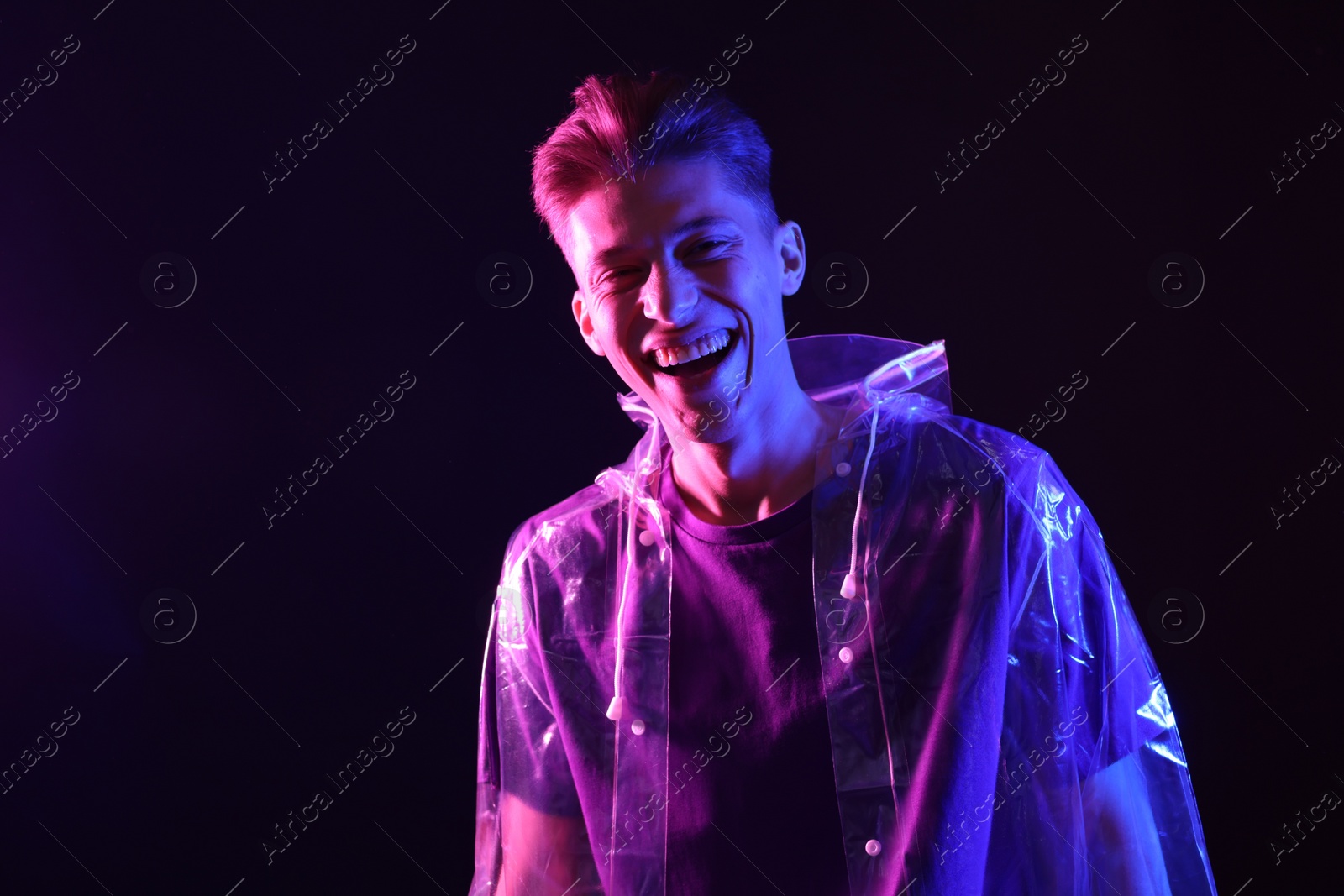 Photo of Young man wearing clear coat on dark background in neon lights. Space for text