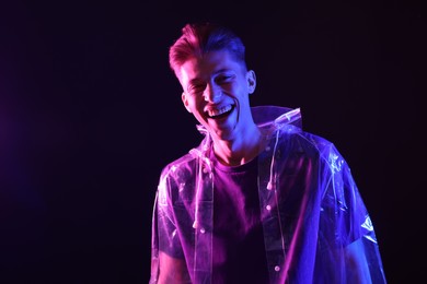 Photo of Young man wearing clear coat on dark background in neon lights. Space for text