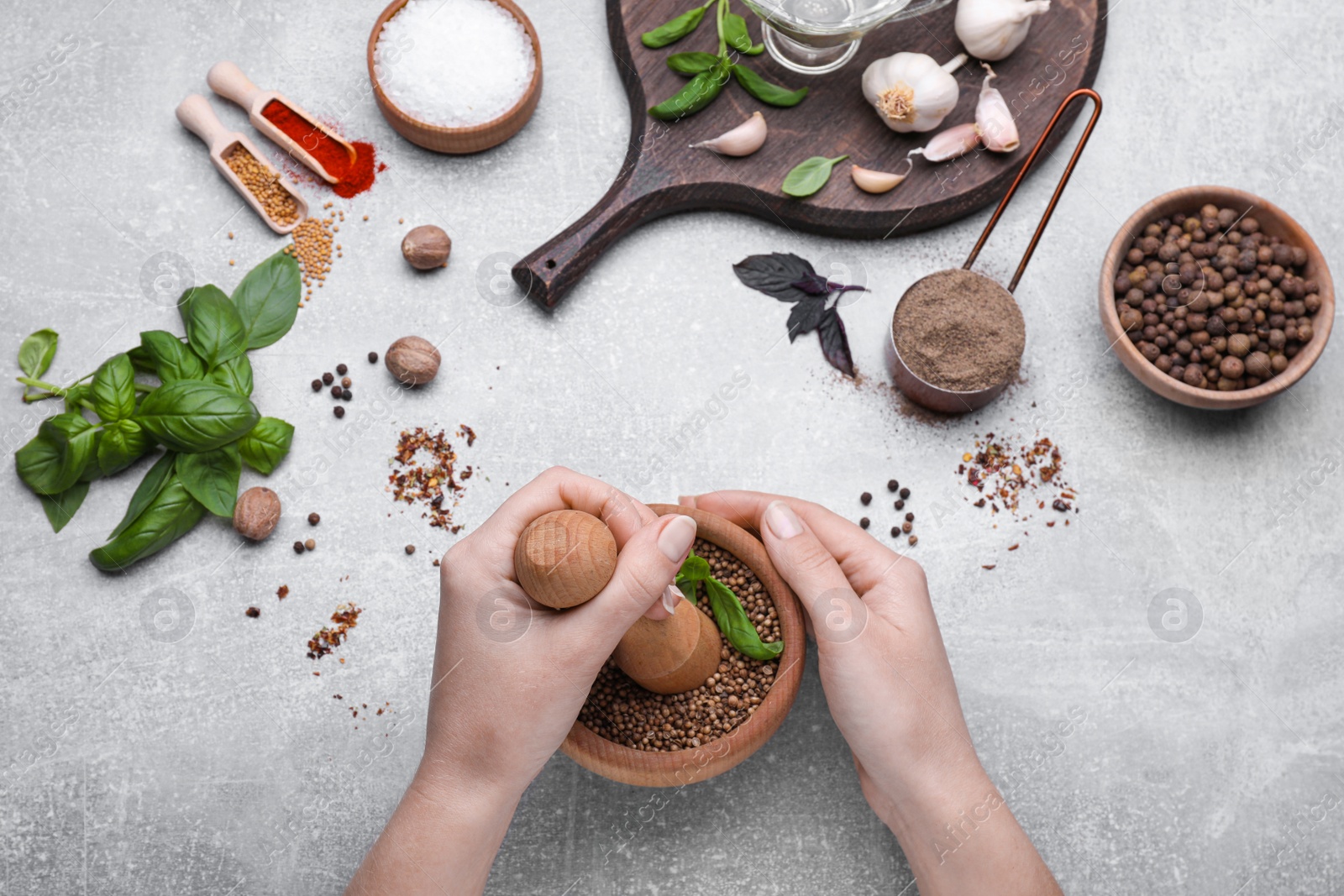 Photo of Woman mixing peppercorns and basil in mortar at light grey table, top view