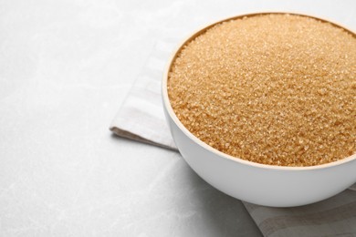 Photo of Brown sugar in bowl on light grey table, closeup. Space for text