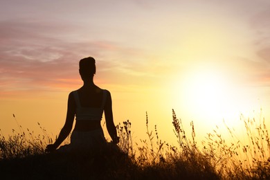Photo of Silhouette of woman meditating outdoors at sunset, back view. Space for text