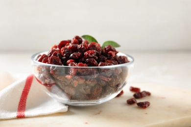 Photo of Dried cranberries in glass bowl on light table, closeup