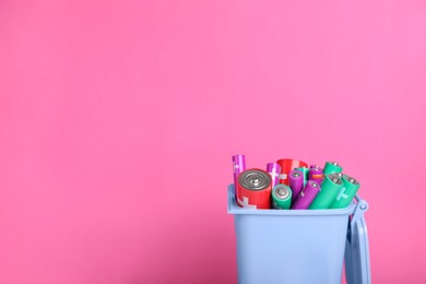 Photo of Many used batteries in recycling bin on pink background. Space for text