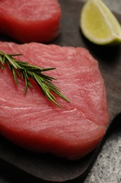 Photo of Raw tuna fillet with rosemary on dark board, closeup