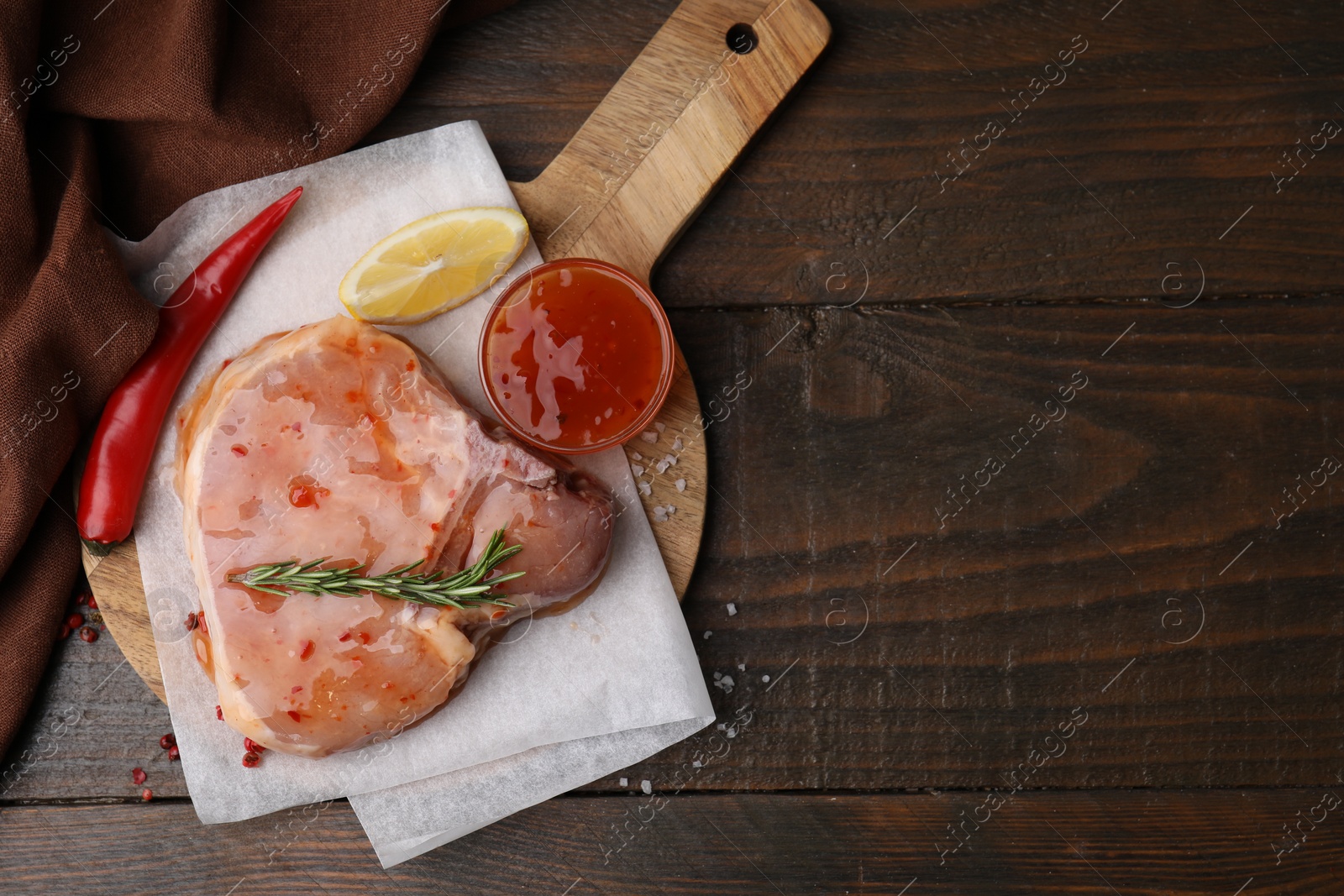 Photo of Board with raw marinated meat, lemon, rosemary and spices on wooden table, top view. Space for text