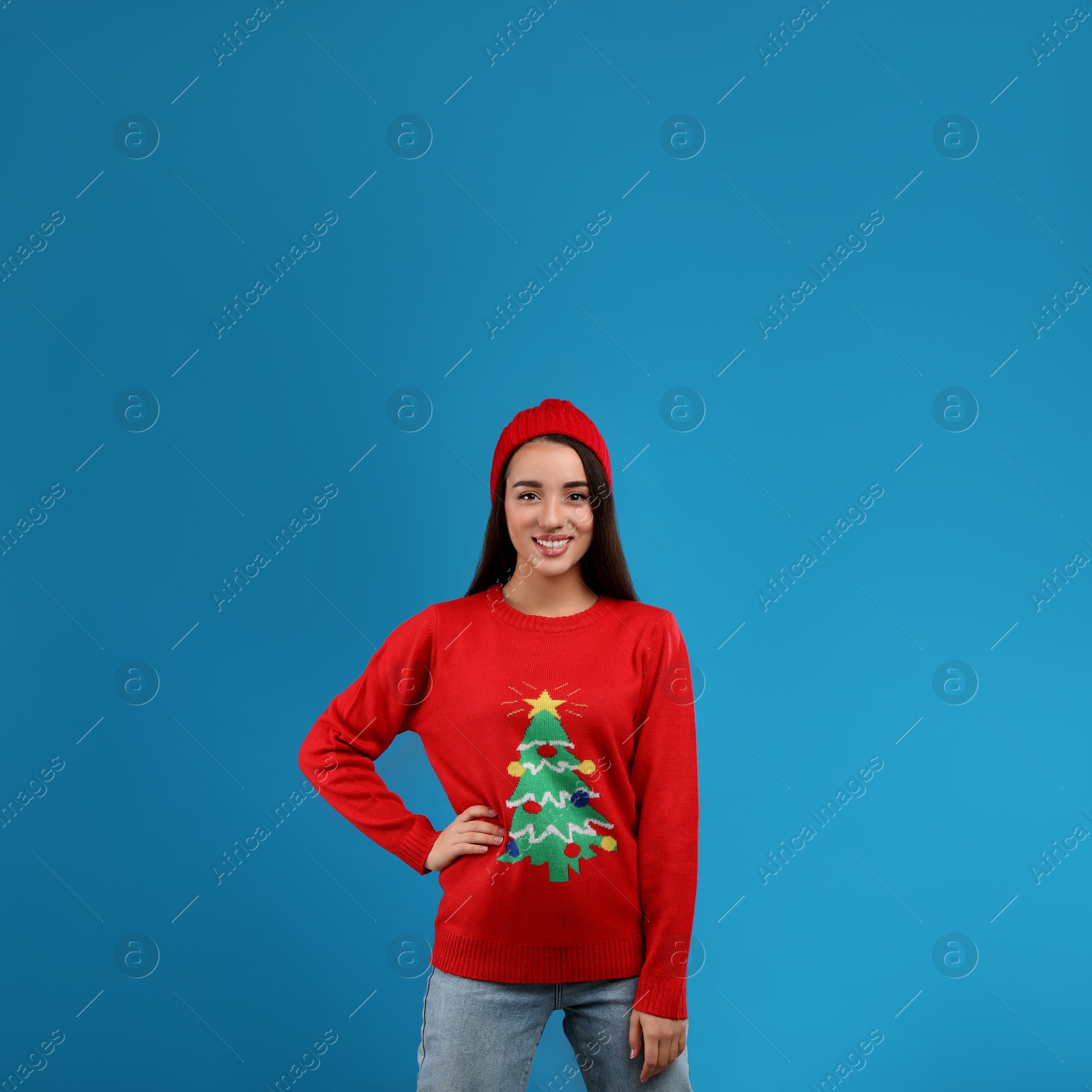 Photo of Young woman in Christmas sweater and hat on blue background, space for text