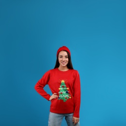 Young woman in Christmas sweater and hat on blue background, space for text