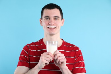 Happy man with milk mustache holding glass of tasty dairy drink on light blue background