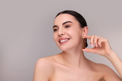 Photo of Beautiful young woman holding skincare ampoule on grey background. Space for text