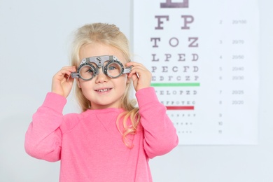 Photo of Little girl with trial frame near eye chart in hospital, space for text. Visiting children's doctor