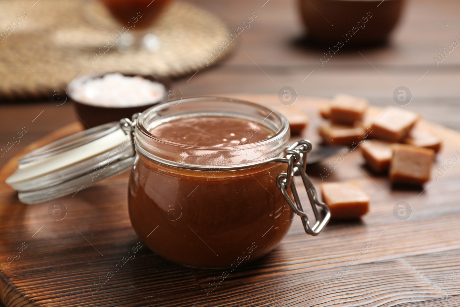 Photo of Jar of tasty caramel sauce on board, closeup