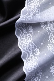 Photo of Beautiful white lace on black fabric, top view