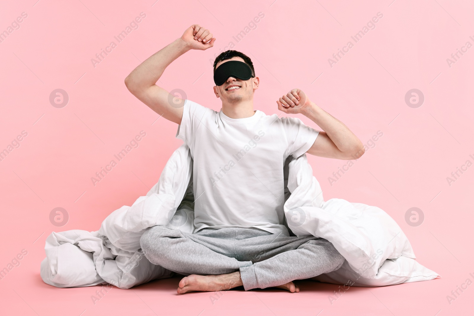 Photo of Happy man in pyjama with sleep mask and blanket on pink background