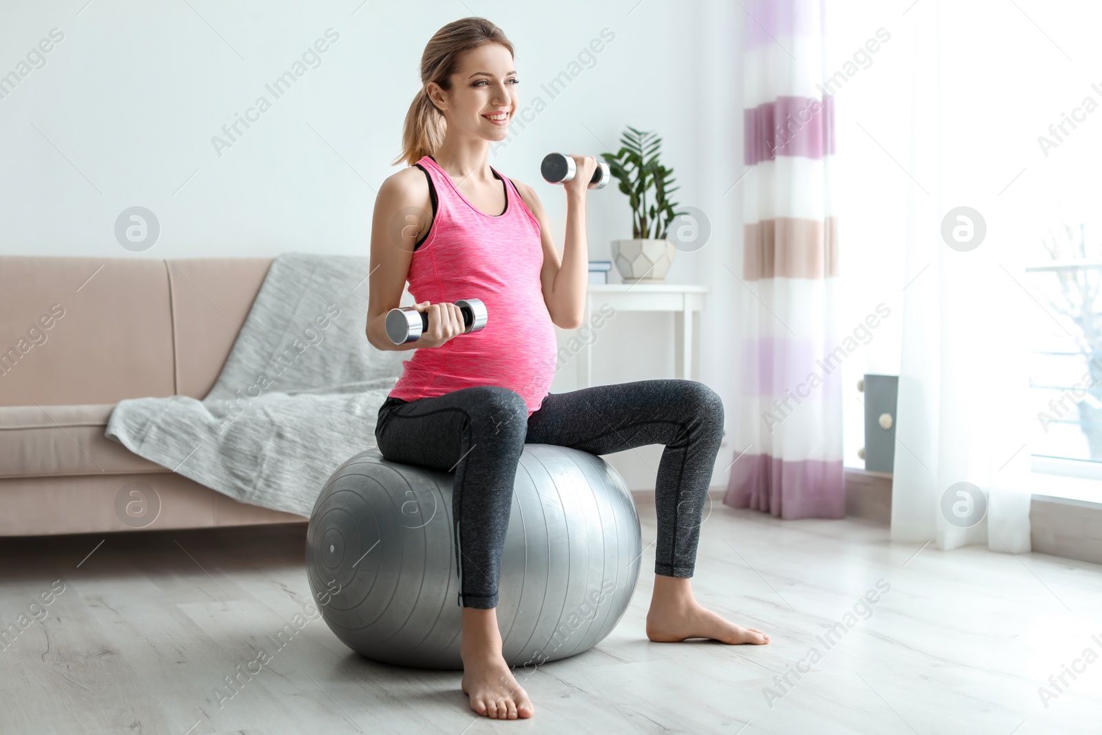 Photo of Young pregnant woman doing exercises with dumbbells at home