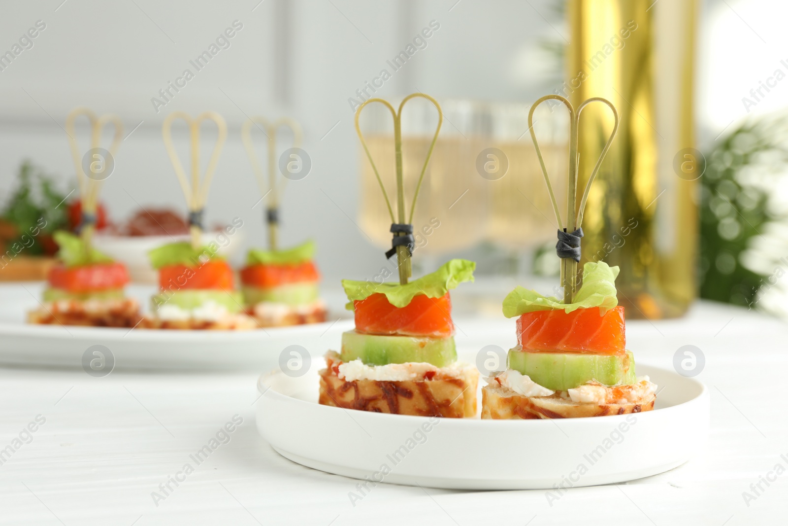 Photo of Tasty canapes with salmon, cucumber, bread and cream cheese on white wooden table