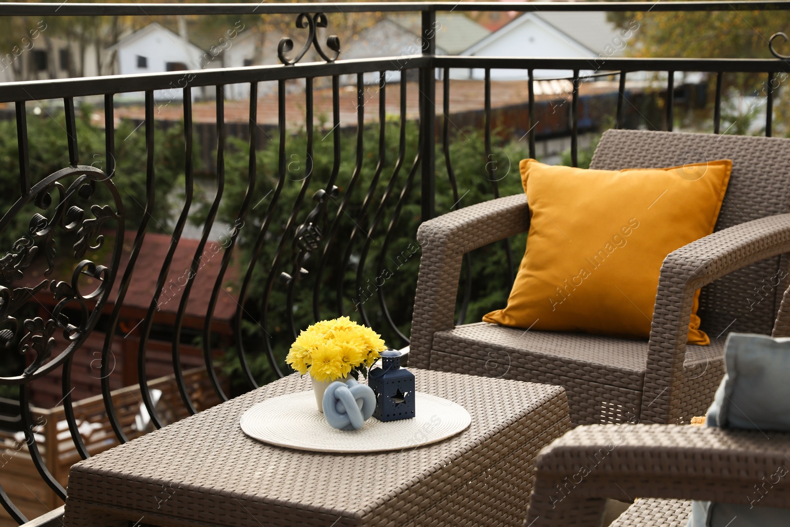 Photo of Orange pillow and yellow chrysanthemum flowers on rattan garden furniture outdoors