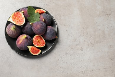 Whole and cut ripe figs with leaf on light grey textured table, top view. Space for text