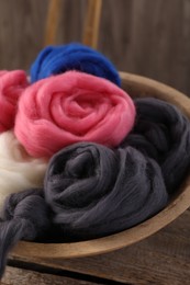 Photo of Colorful felting wool in bowl on wooden table, closeup