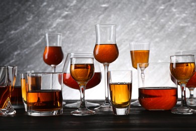 Photo of Different delicious liqueurs in glasses on dark wooden table