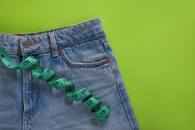 Photo of Jeans and measuring tape on light green background, top view with space for text. Weight loss concept