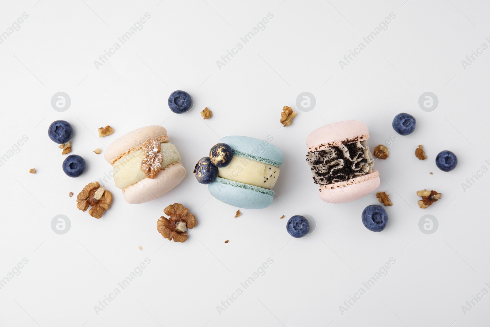 Photo of Delicious macarons, walnuts and blueberries on white table, flat lay