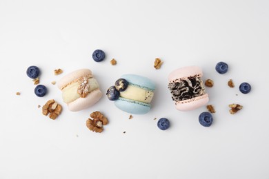 Delicious macarons, walnuts and blueberries on white table, flat lay