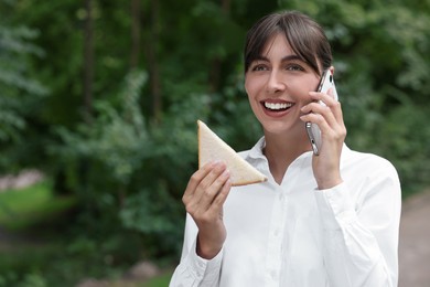 Photo of Lunch time. Happy businesswoman with sandwich talking on smartphone outdoors, space for text