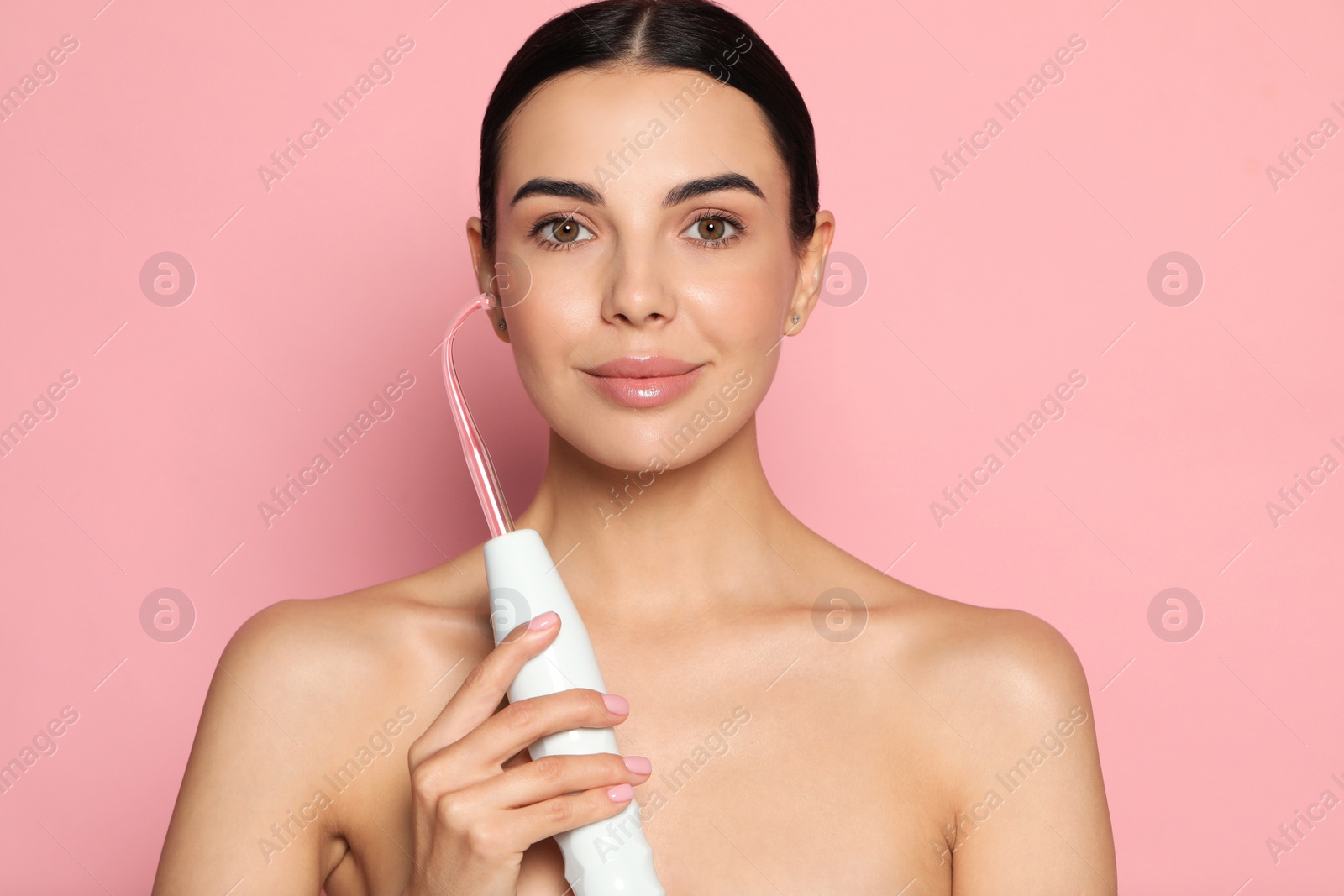 Photo of Woman using high frequency darsonval device on pink background. Space for text