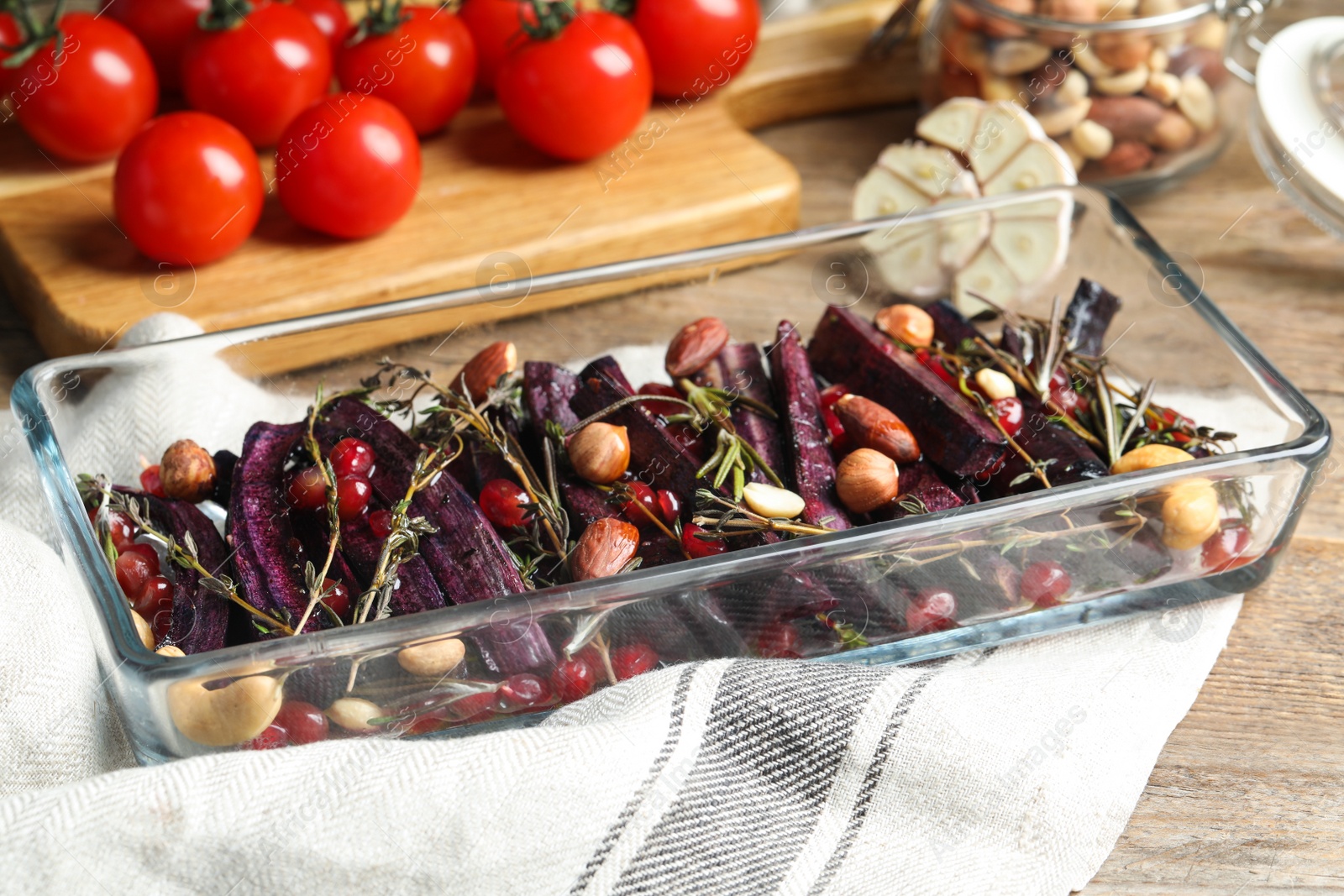 Photo of Baked black carrot with pomegranate seeds and nuts on wooden table, closeup