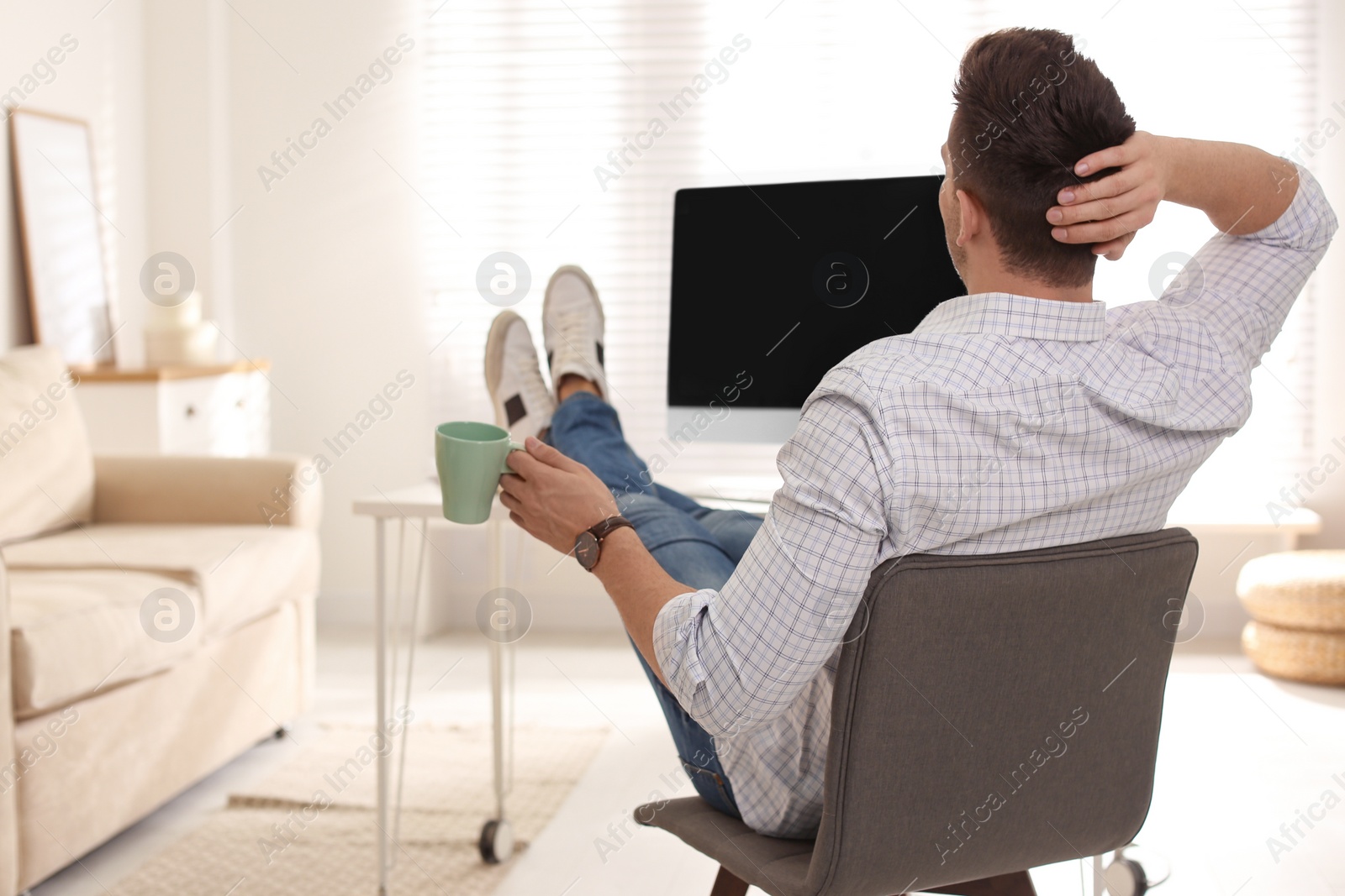 Photo of Young man with cup of drink relaxing at table in office during break