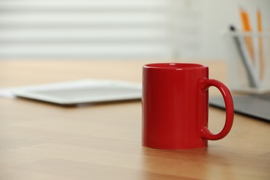 Photo of Red ceramic mug on wooden table at workplace. Mockup for design