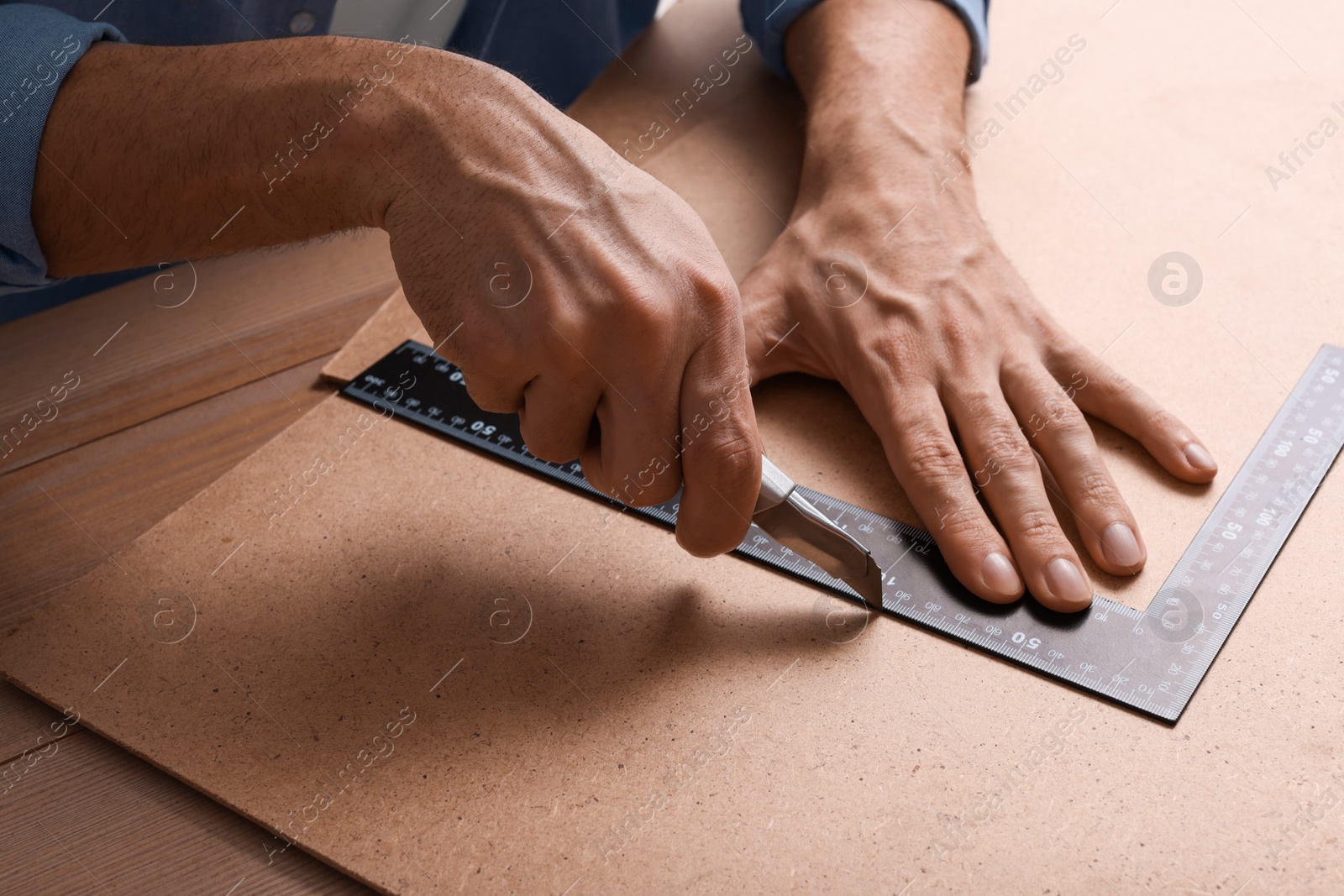 Photo of Man cutting chip board with utility knife and ruler at table, closeup