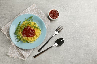 Photo of Tasty spaghetti squash with tomato sauce and arugula served on light grey table, flat lay. Space for text