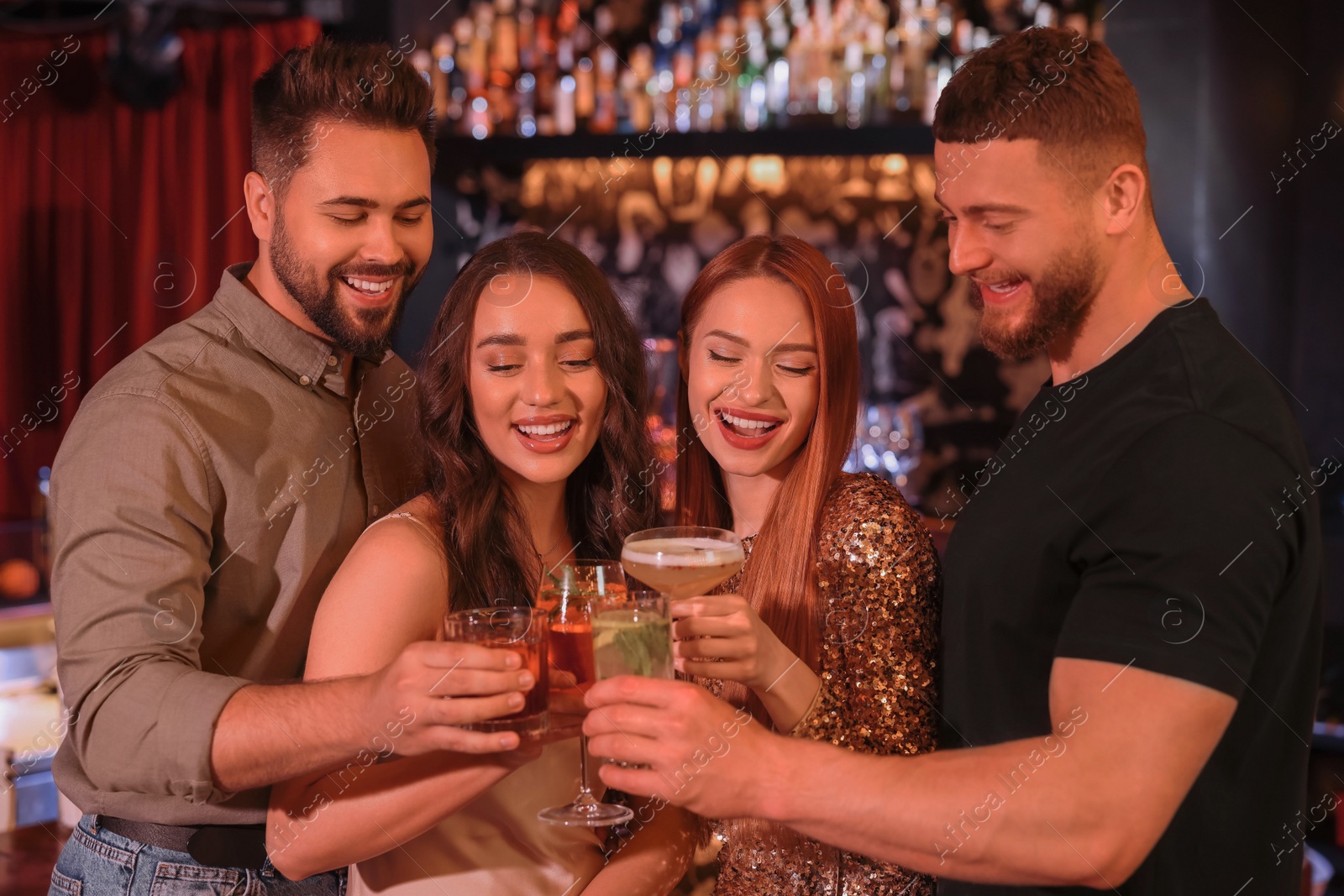 Photo of Happy friends clinking glasses with fresh cocktails in bar